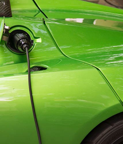 Green electric car charging: Close-up of indistinguishable electric car 'fueling', i.e. plugged to the electricity hose, charging battery.